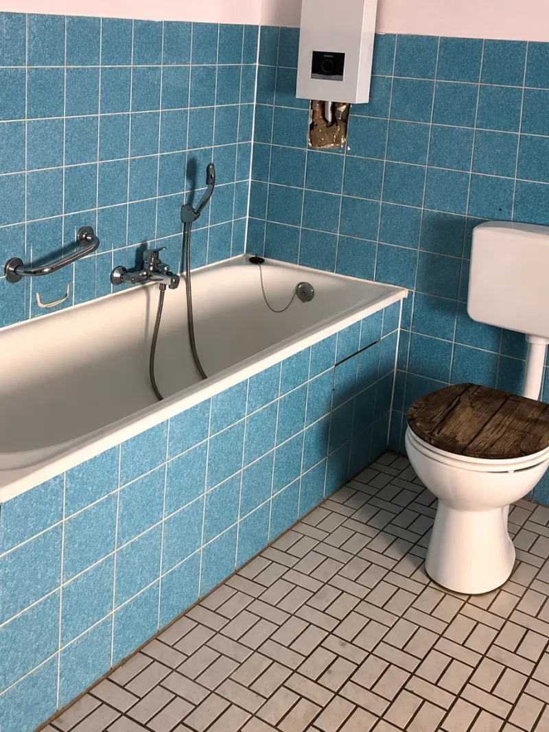 Bathroom with teal wall tiles, a bathtub and a toilet