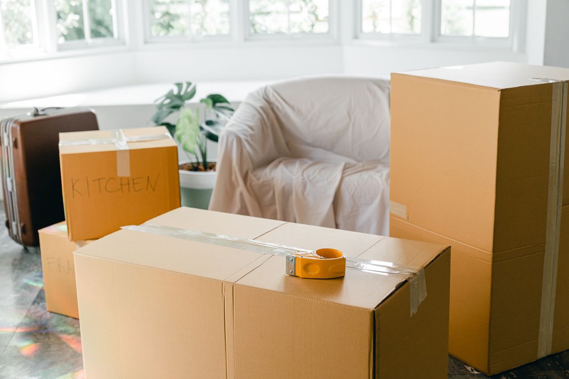 Bright living room with sealed moving boxes, a suitcase and a covered armchair
